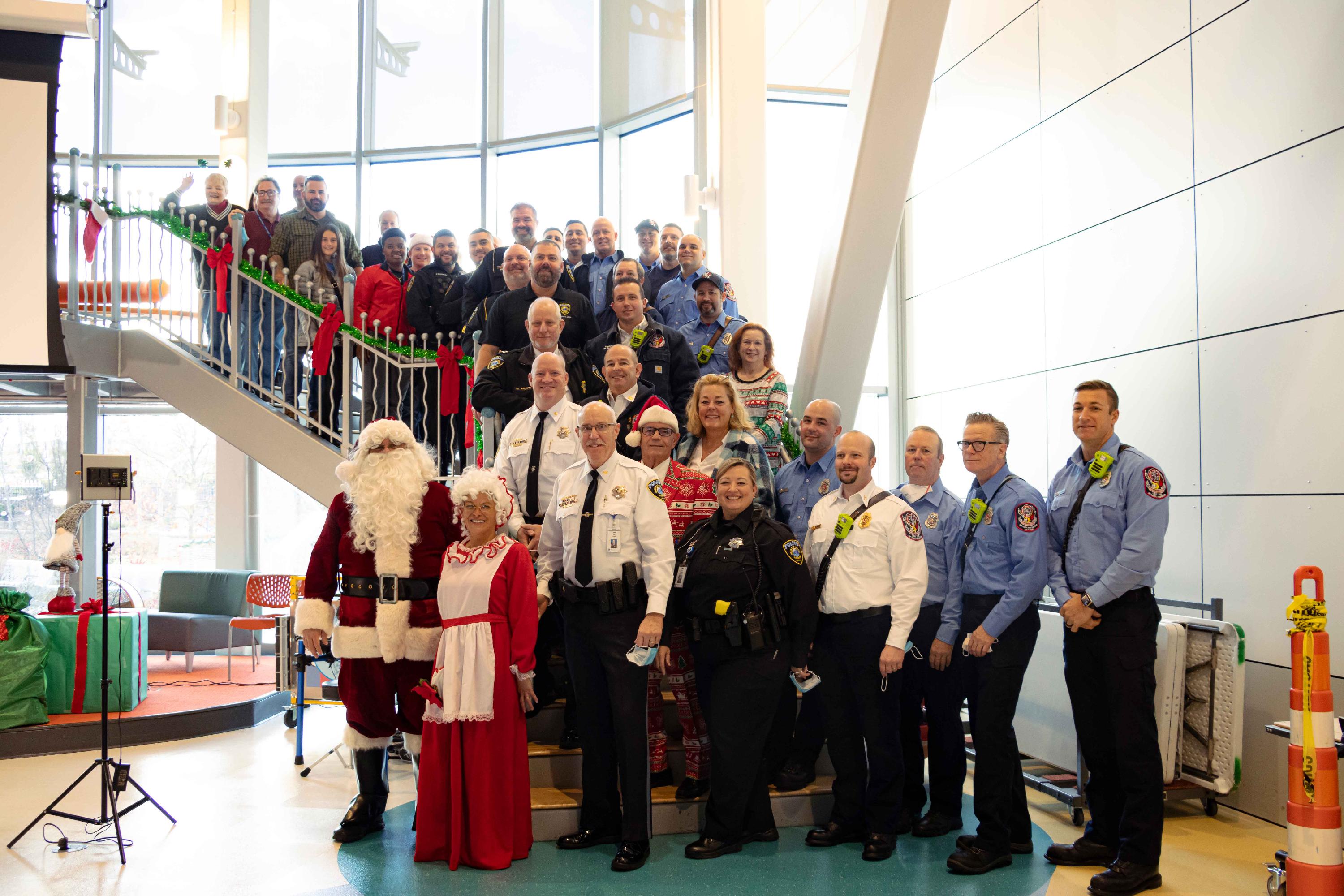 Santa, Mrs. Claus, and members of the Maryland Heights Police Department, Maryland Heights Fire Protection District, and Maryland Heights Government pose for a photo on a staircase at Ranken Jordan Pediatric Bridge Hospital